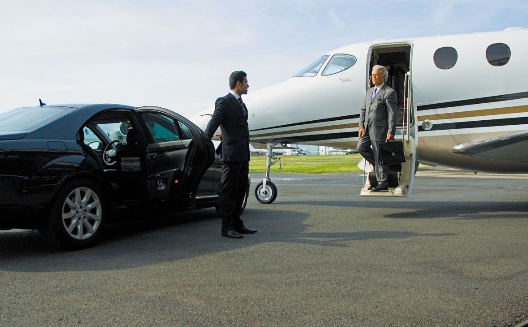 Airport Transportation Services with a chauffeur holding the car door as a businessman steps down from a private jet on the runway.
