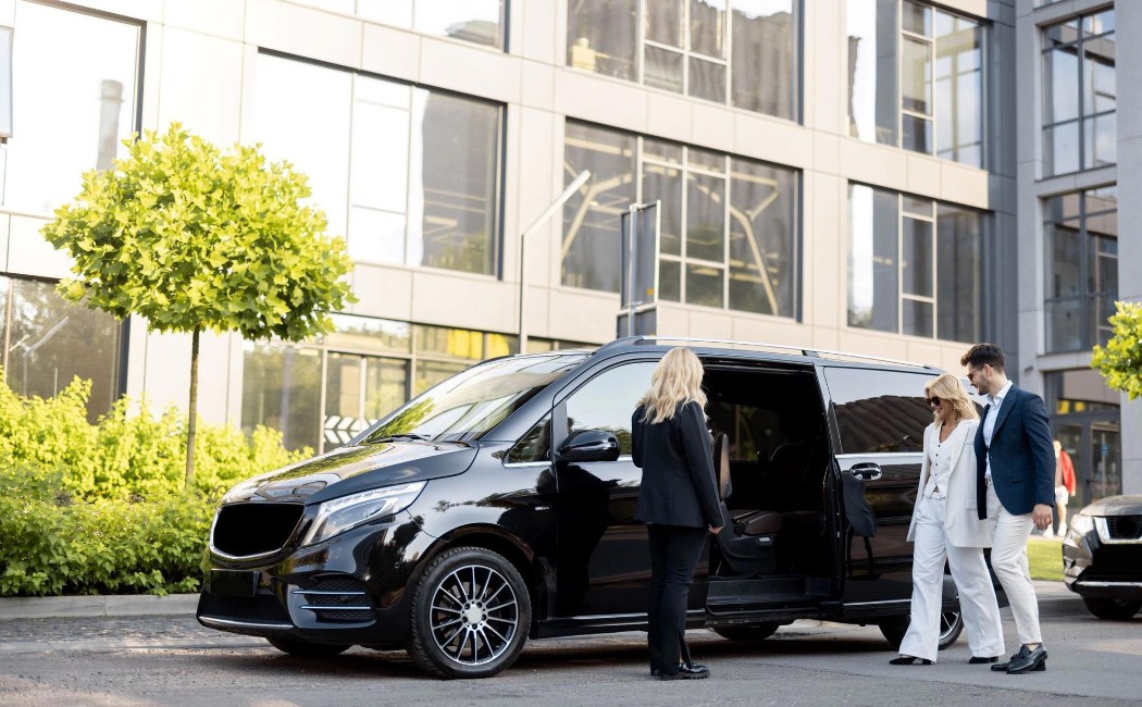 Professional chauffeur assisting well-dressed clients into a luxury black van outside a modern building, offering premium Special Event Rides for corporate and formal occasions.