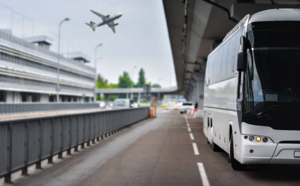 Airport Transportation Services featuring a modern shuttle bus parked at the terminal curbside with an airplane flying overhead.