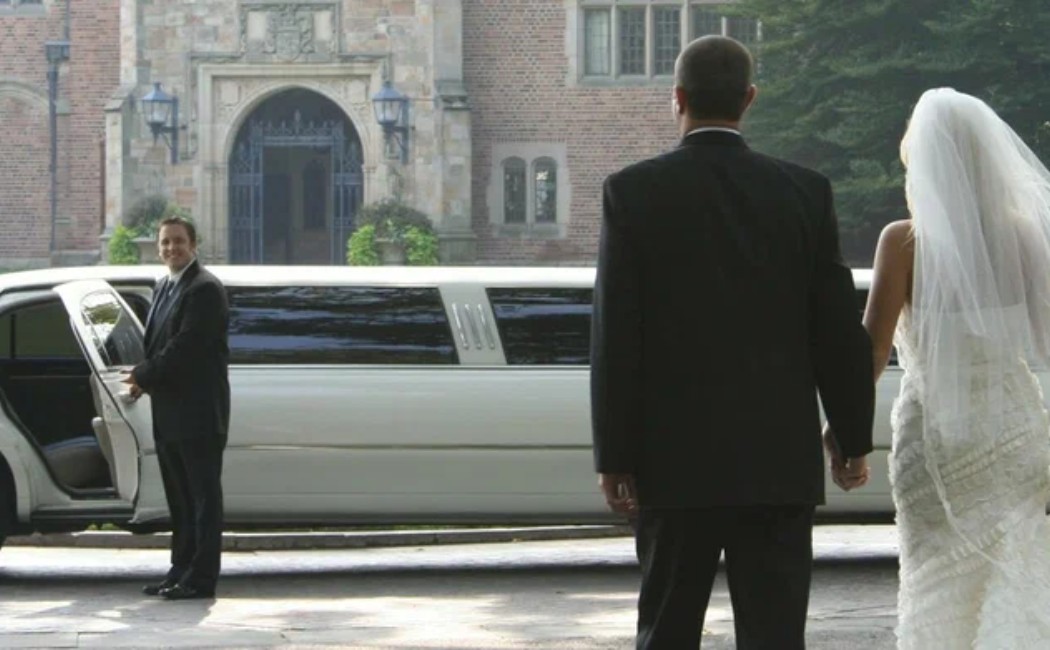 Bride and groom holding hands as they approach a white limousine outside a grand venue, showcasing elegant Wedding Transportation Services.