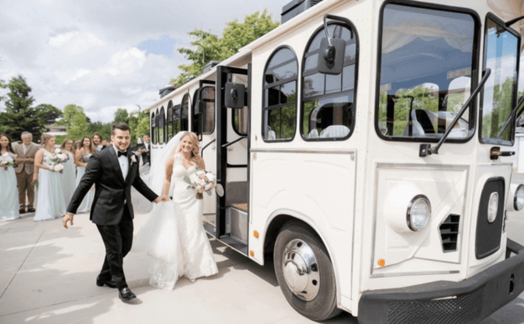 Bride and groom stepping off a vintage white trolley bus while wedding guests follow behind outdoors.

Elegant Wedding Transportation provides a charming and stylish arrival for the celebration.